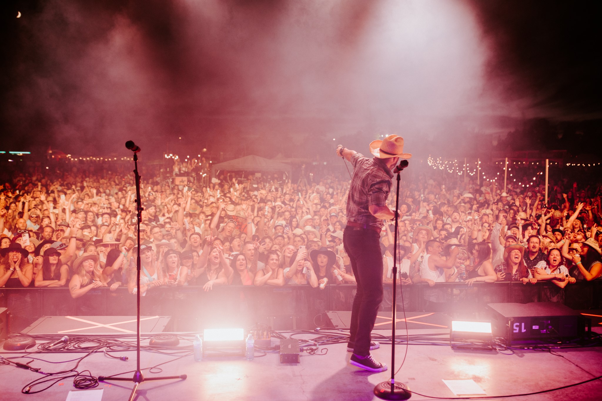 An artist stands on stage holding his mic out to the audience as they sing his song.