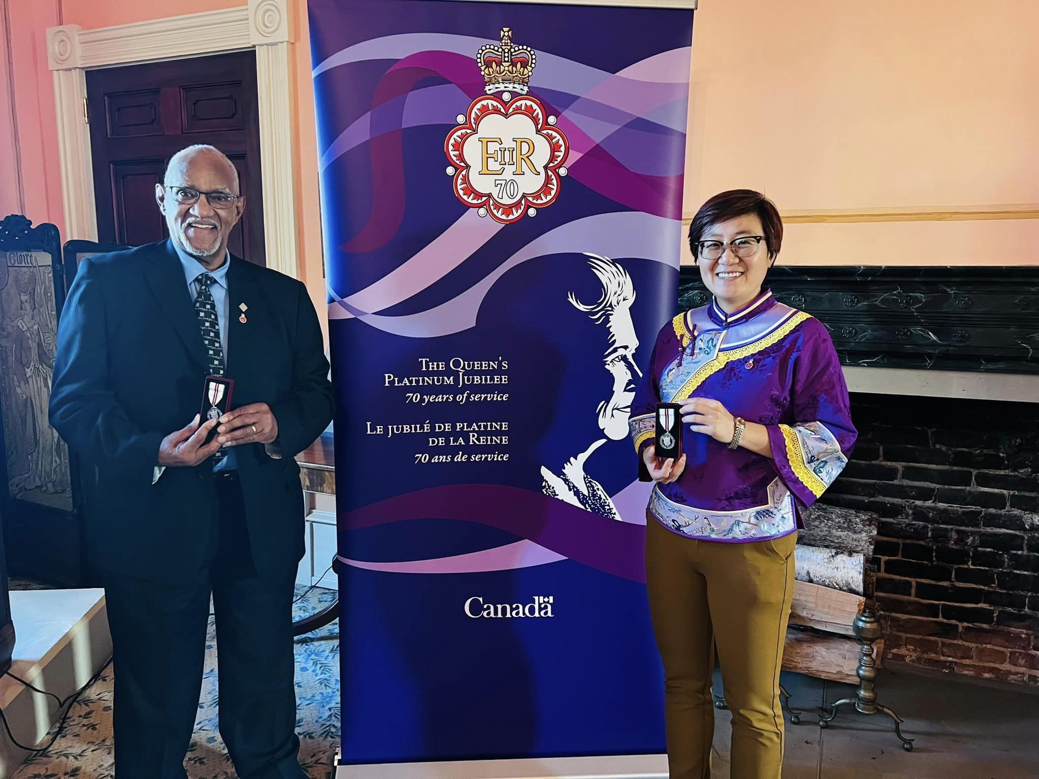 Li tient sa médaille à côté d'une bannière sur laquelle on peut lire « Le jubilé de platine de la reine – 70 ans de service ».