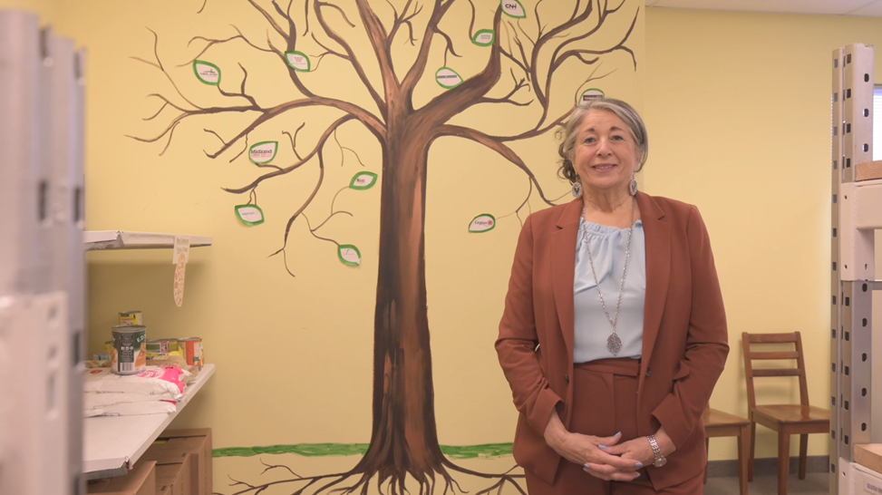 •	Grace, souriante, pose devant la murale représentant un arbre qu’elle a peinte dans les locaux du Georgian Bay Food Network.