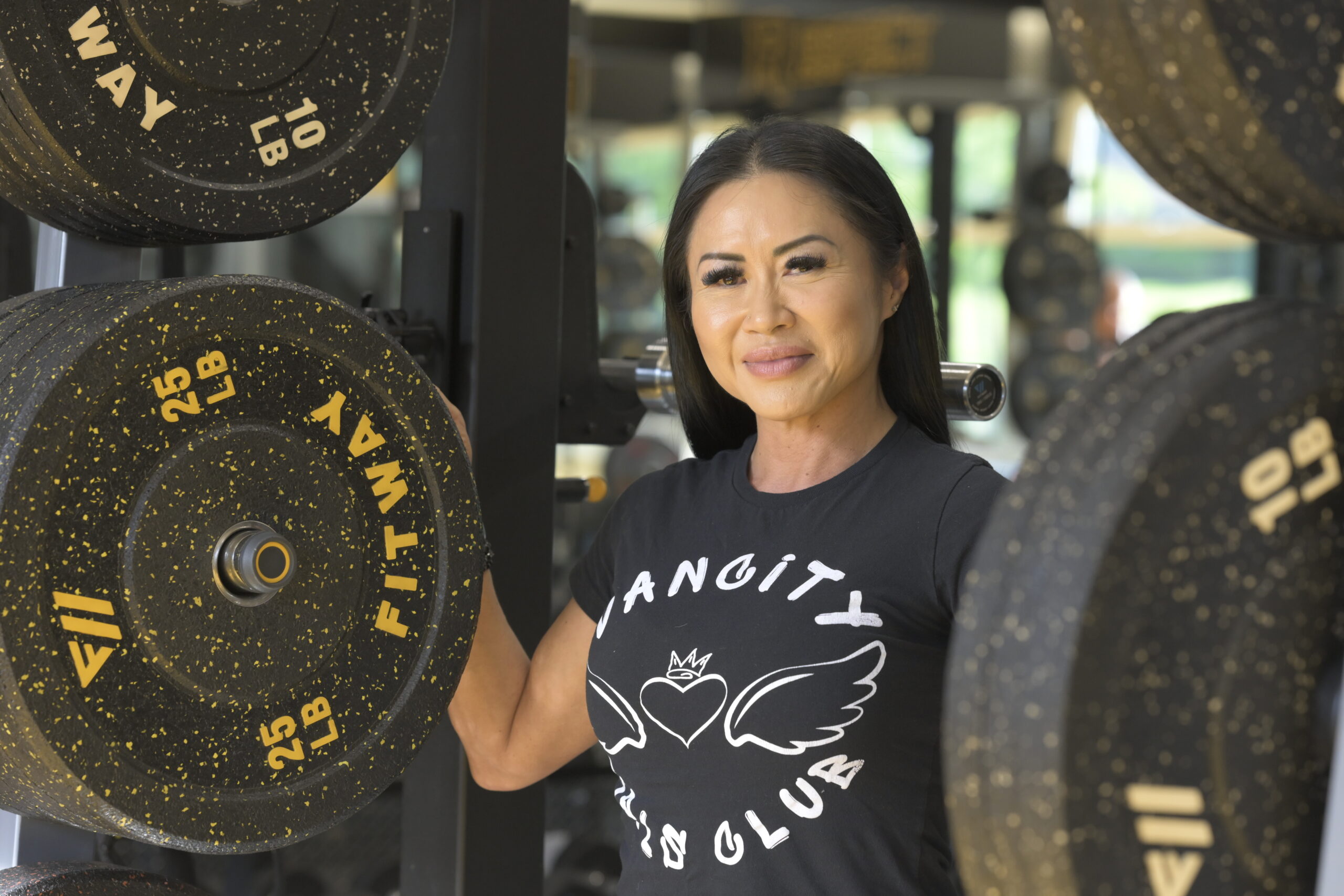 Juliana stands proudly between barbell weights in a Vancity Girls Club t-shirt -- Juliana se tient fièrement entre les poids d'haltères dans un t-shirt Vancity Girls Club