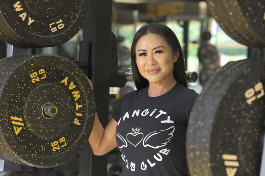 Juliana stands proudly between barbell weights in a Vancity Girls Club t-shirt -- Juliana se tient fièrement entre les poids d'haltères dans un t-shirt Vancity Girls Club